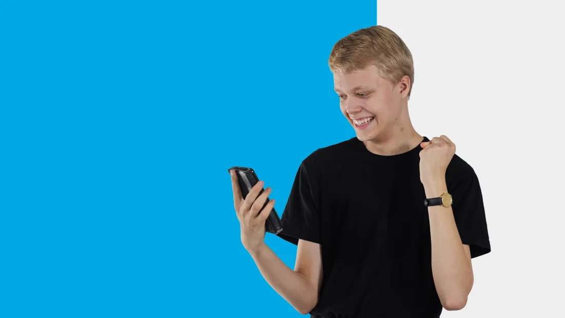 Nuori mies katsoo innostuneen näköisenä kännykkää.