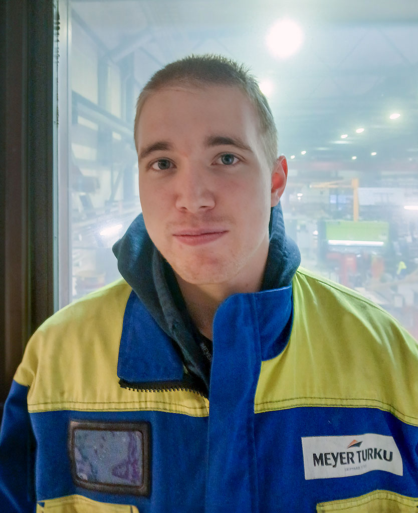 Nuori mies kelta-sinisissä työvaatteissa, takin rintapielessä Mayerin logo.