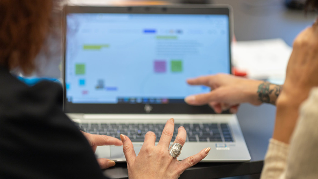 Kaksi henkilöä tutkii sumennettua kalenterinäkymää tietokoneen ruudulla.