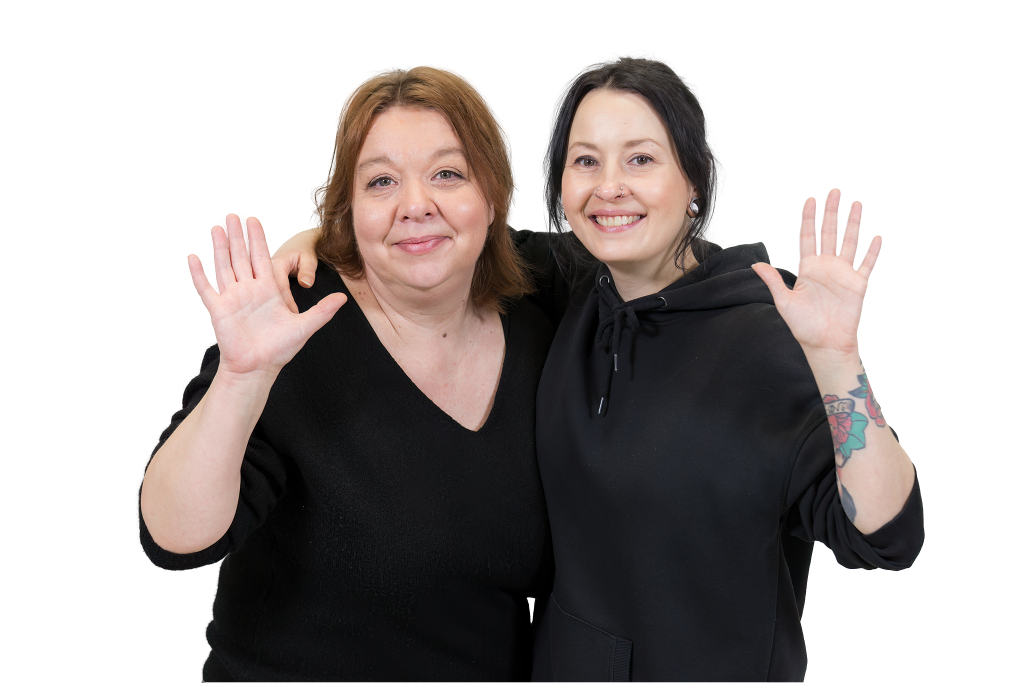 Kaksi hymyilevää naista moikkaa.