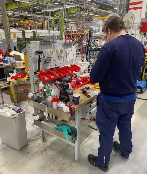 Nuori mies töissä suuressa teollisuustilassa, jossa paljon laitteita ja yksityiskohtia.