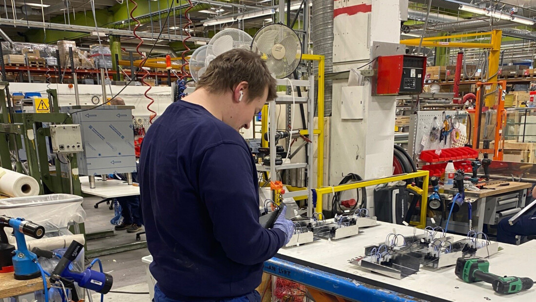 Nuori mies tutkii keskittyneesti jotain, taustalla suuri teollinen tila.