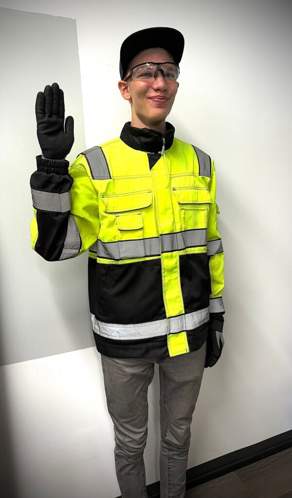 Henkilö työvaatteet päällään heiluttaa hymyilevästi. 