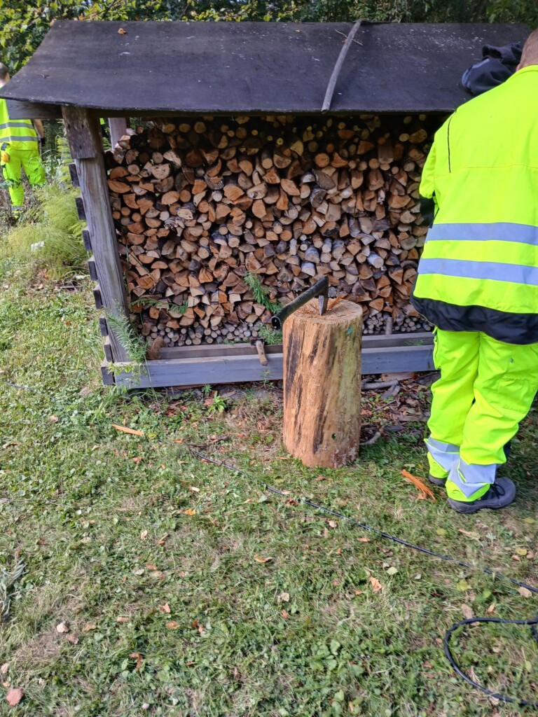 Henkilö kasaa halkoja ulkona suojaan työvaatteet päällään. 
