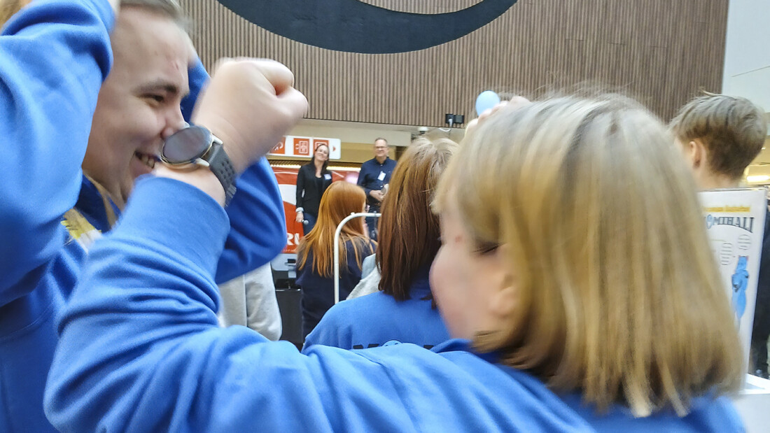 Kaksi nuorta tuulettaa iloisesti, päällä siniset hupparit, taustalla kauppakeskus.