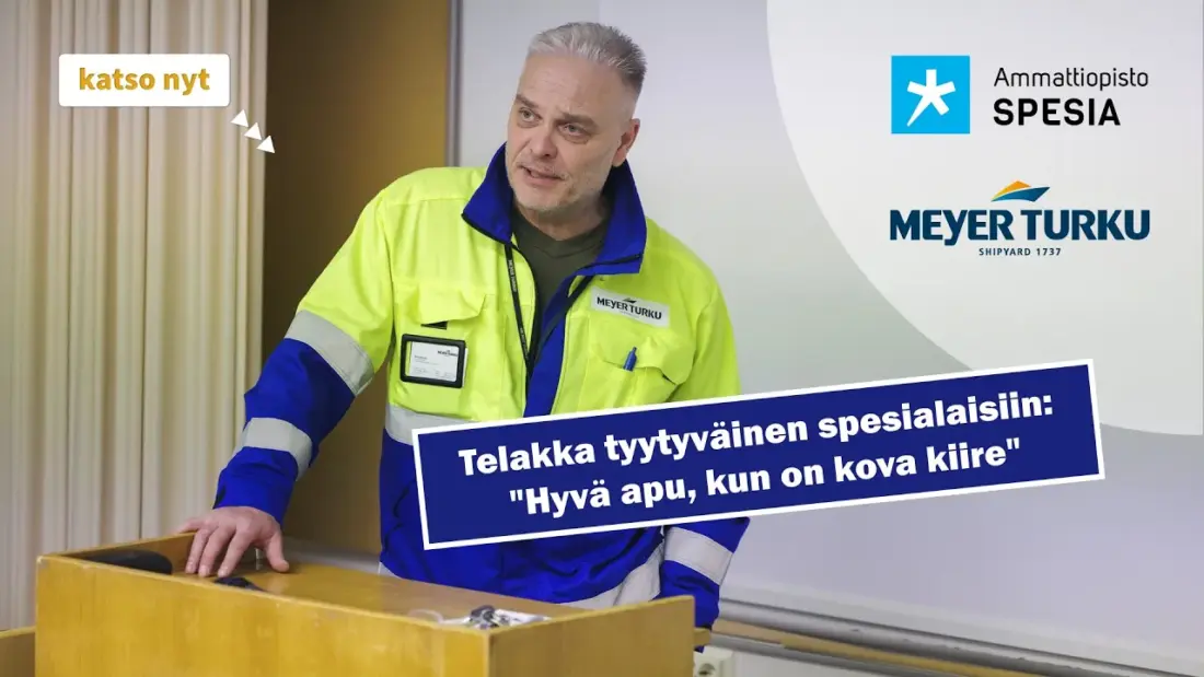 Turvallisuusliiviä käyttävä henkilö seisoo puhujapöydän ääressä sisätilassa. Kuvassa näkyvät Meyer Turku -telakan ja Ammattiopisto Spesian logot. Etualalla on sininen tekstibanneri, jossa lukee: "Telakka tyytyväinen spesialaisiin: Hyvä apu, kun on kova kiire". Vasemmassa yläkulmassa on keltainen painike, jossa teksti "katso nyt".