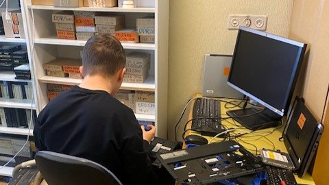 Opiskelija istuu yrityksen työhuoneessa, jossa on tietokoneita ja tietokoneen korjaamiseen tarvittavia työkaluja ympärillään.