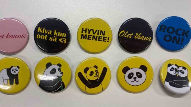 Värikkäitä pinssejä rivissä pöydällä eri kuvilla ja teksteillä. 