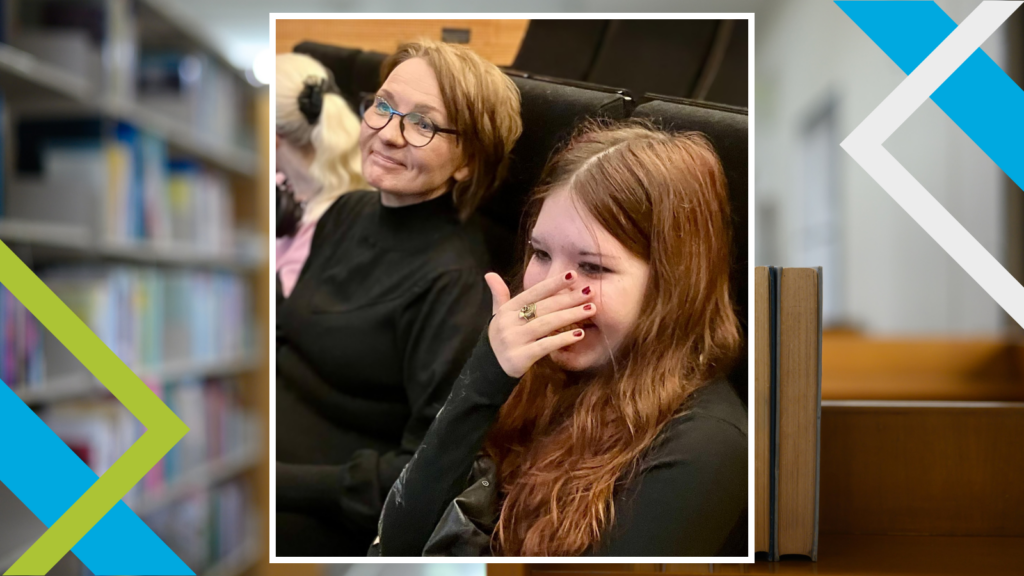 Nuori ja aikuinen istuvat katsomossa, nuorta näyttää naurattavan, taustalla näkymä kirjastoon.