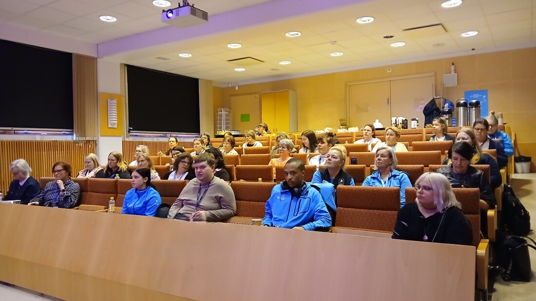 Ihmisiä istuu auditoriossa ja kuuntelee esitystä.