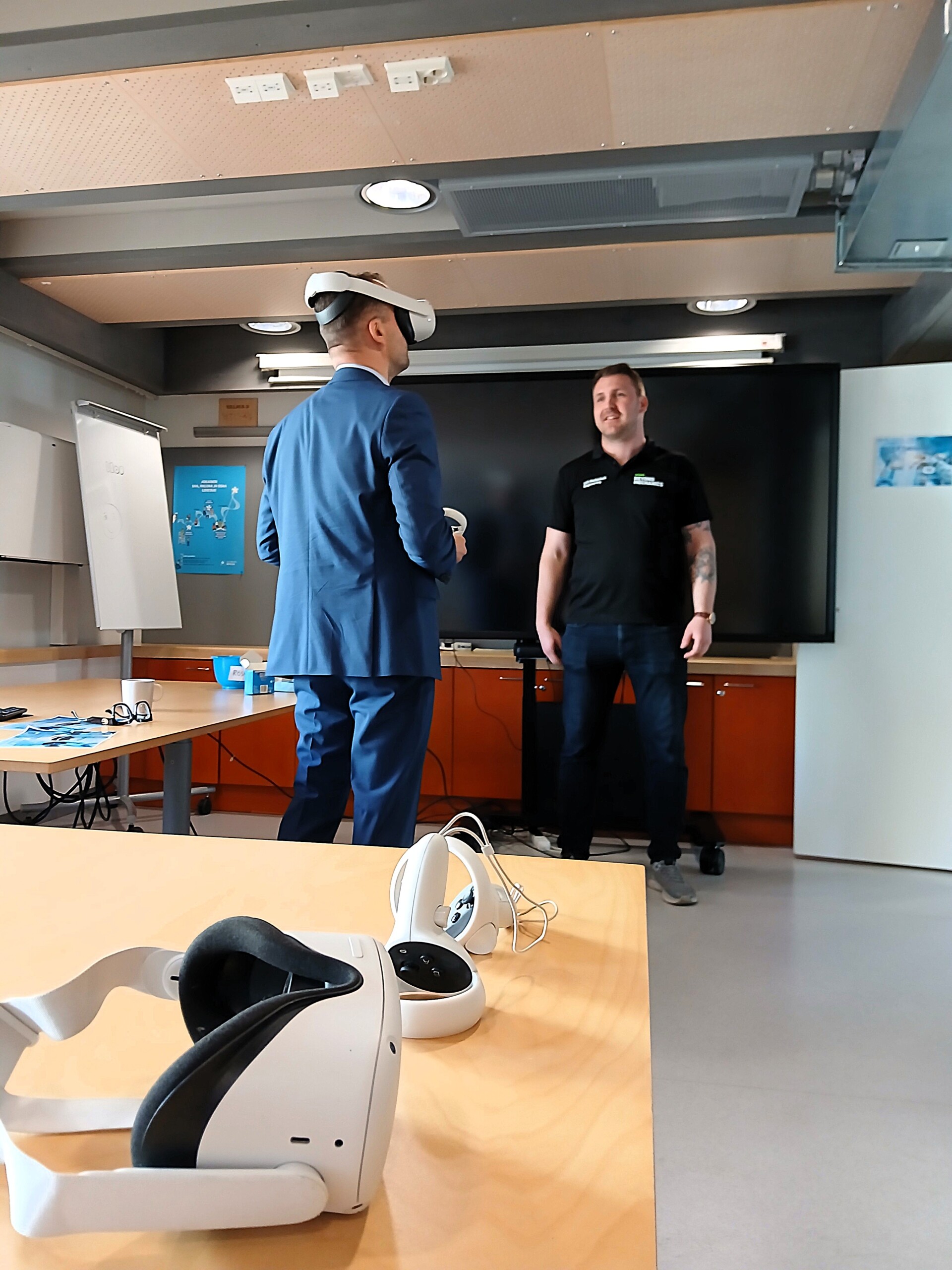 Henkilö seisoo VR-lasit päässään ja toinen henkilö opastaa käytössä vieressä. 