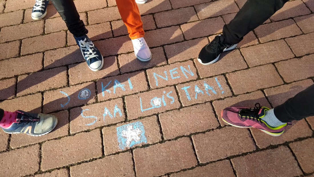jalkoja ringissä asfaltilla. Ringin keskellä teksti "Jokainen saa loistaa".