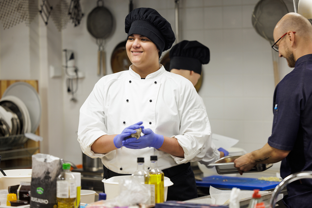Nuori kokkiasussa leipomassa, hymyilee.