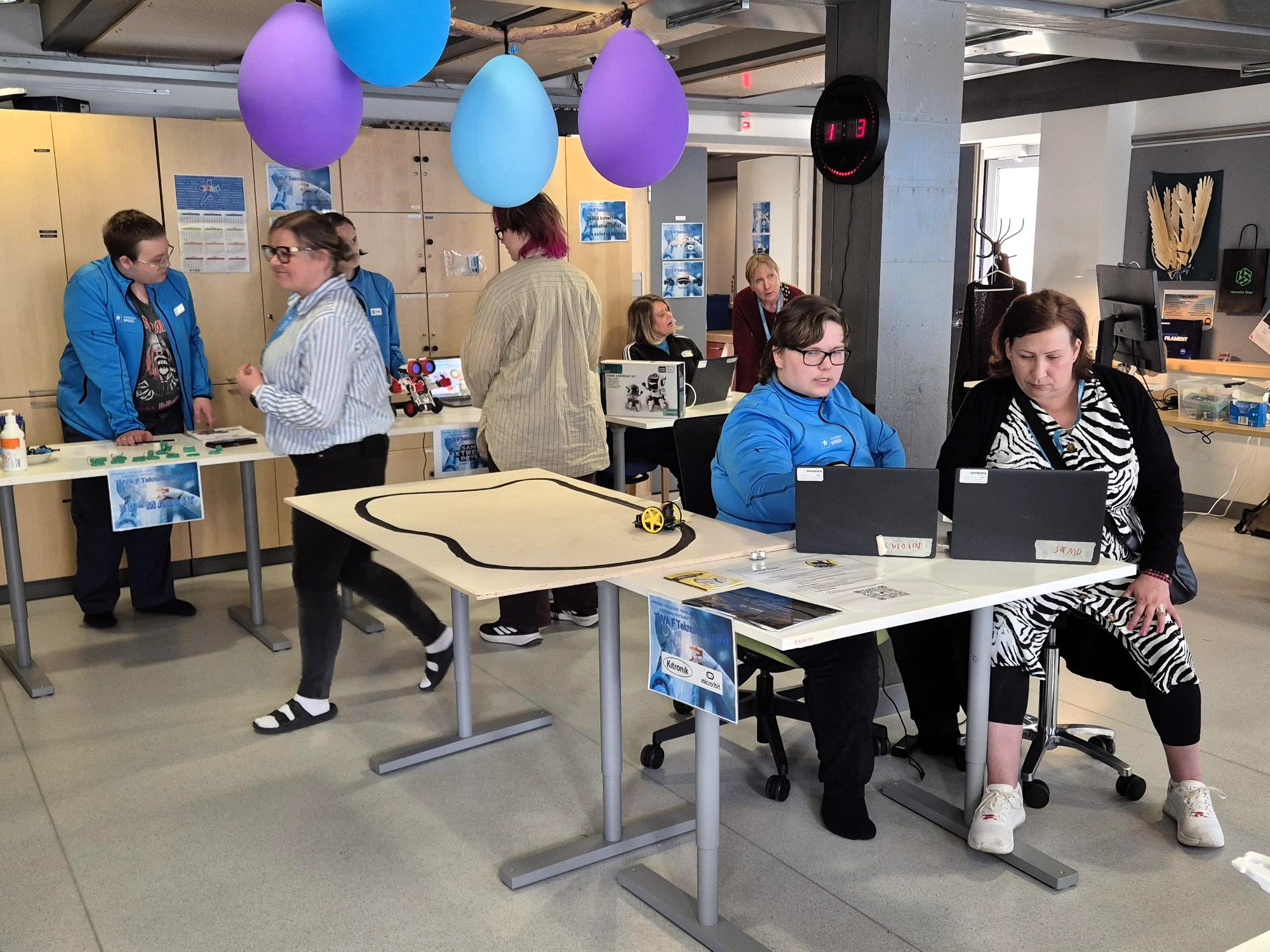 Opiskelijoita, henkilökuntaa ja vieraita luokassa tutustumassa messupisteisiin. 