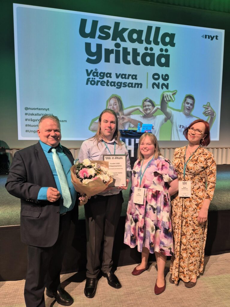 Neljä henkilöä seisoo rivissä ja yhdellä on kasissään kukkakimppu ja kunniakirja. 