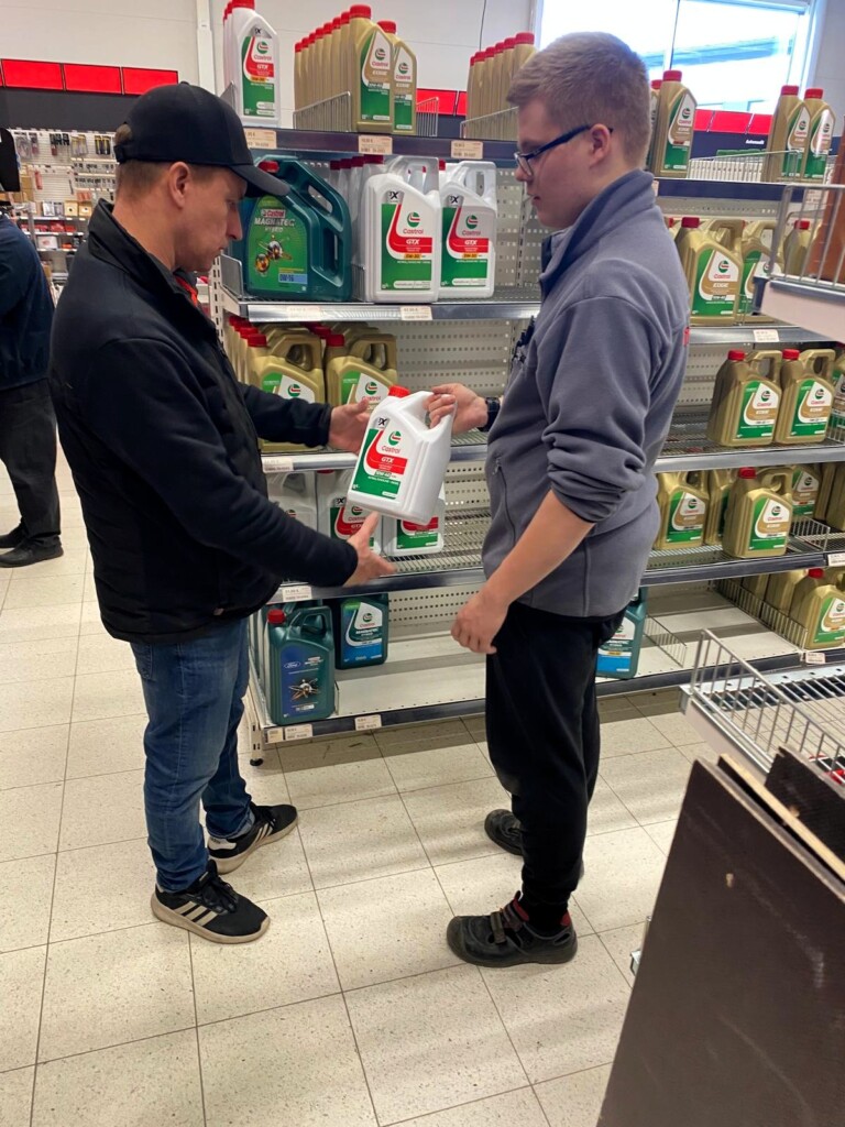 Opiskelija auttaa asiakasta Motonetin käytävällä moottoriöljyjen kanssa. 