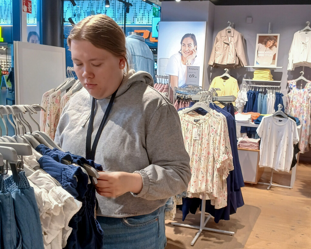 Henkilö asettelee vaatteita vaatekaupan rekissä.