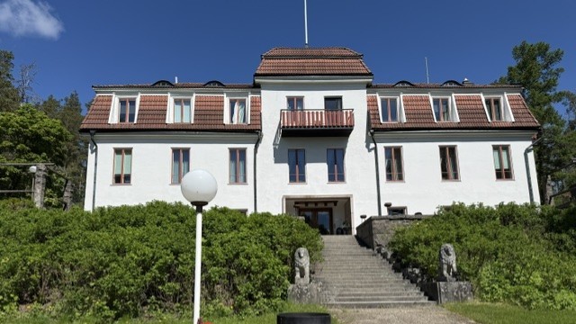 Kaksikerroksisen kivikartanon julkisivu ja pääsisäänkäynti ulkoapäin.