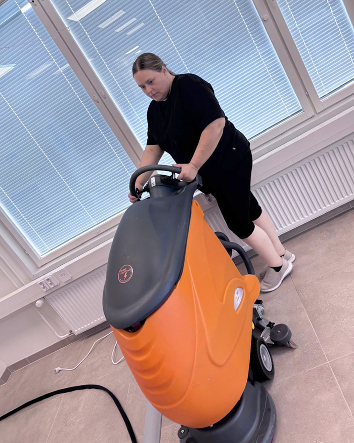 Nainen työntää lattianpesukonetta tyhjässä luokkahuoneessa.