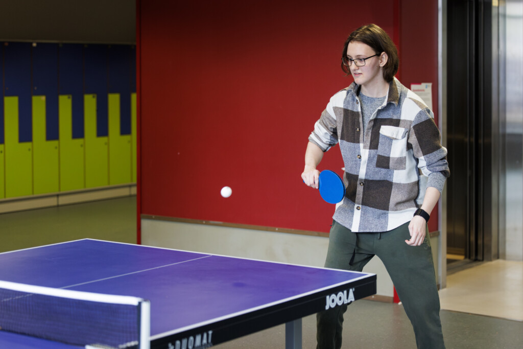 Henkilö pelaa pöytätennistä oppilaitoksen yhteisessä tilassa.