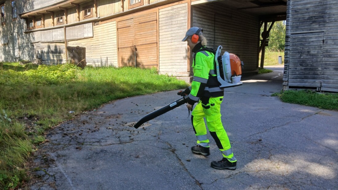 Henkilö puhaltaa lehtiä lehtipuhaltimella ulkona.