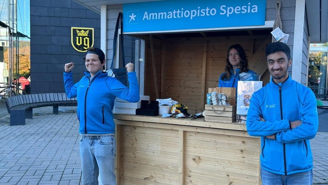 Kolme henkilöä Ammattiopisto Spesian myyntikojun luona Naantalissa. Kojun tiskillä on myyntituotteita ja esittelymateriaalia.